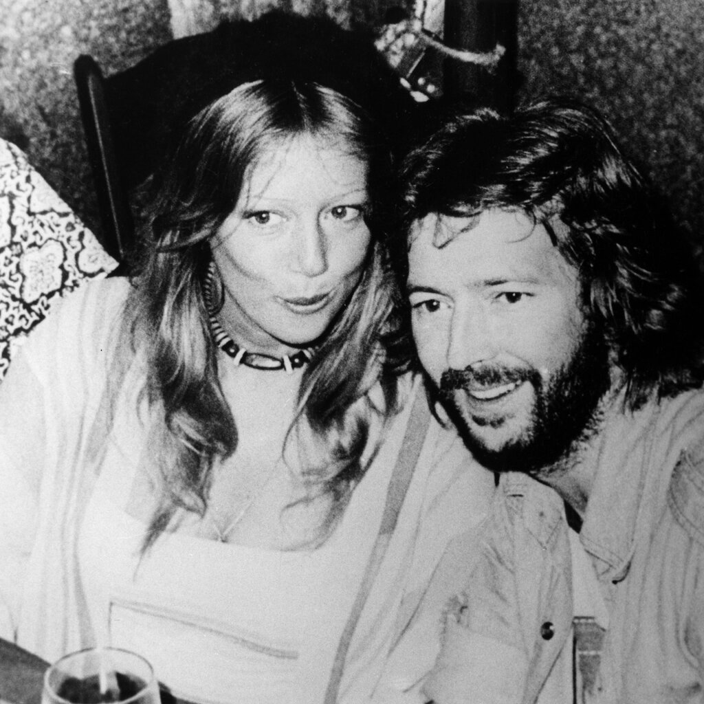 A black-and-white photo shows Pattie Boyd, wearing a dress, and Eric Clapton, wearing a shirt, smiling.