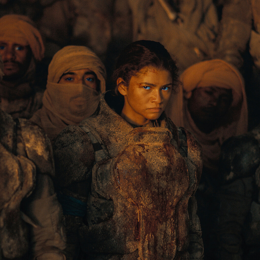 In a crowd of people wearing earth-toned clothing, Zendaya stands out with glowing blue eyes.
