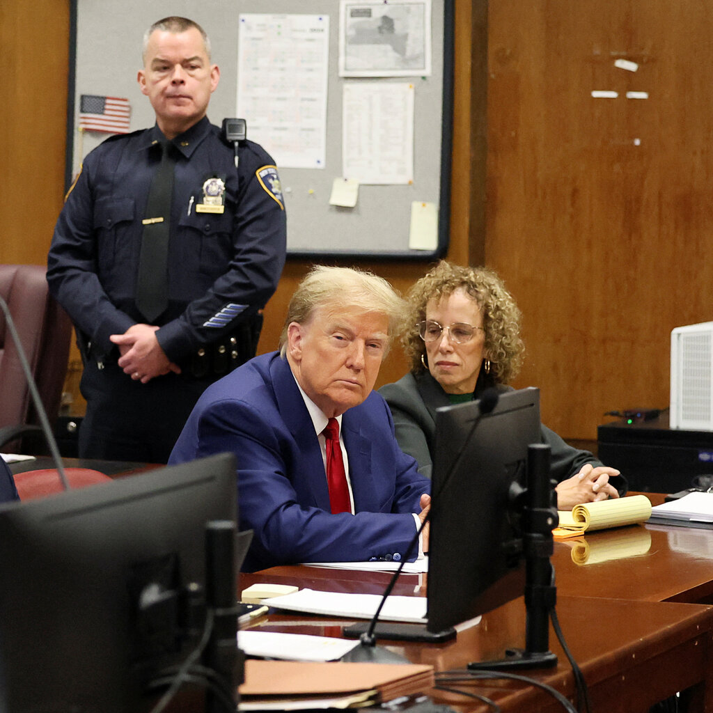 Former President Donald Trump sits at a desk in court, his fingers interlaced.