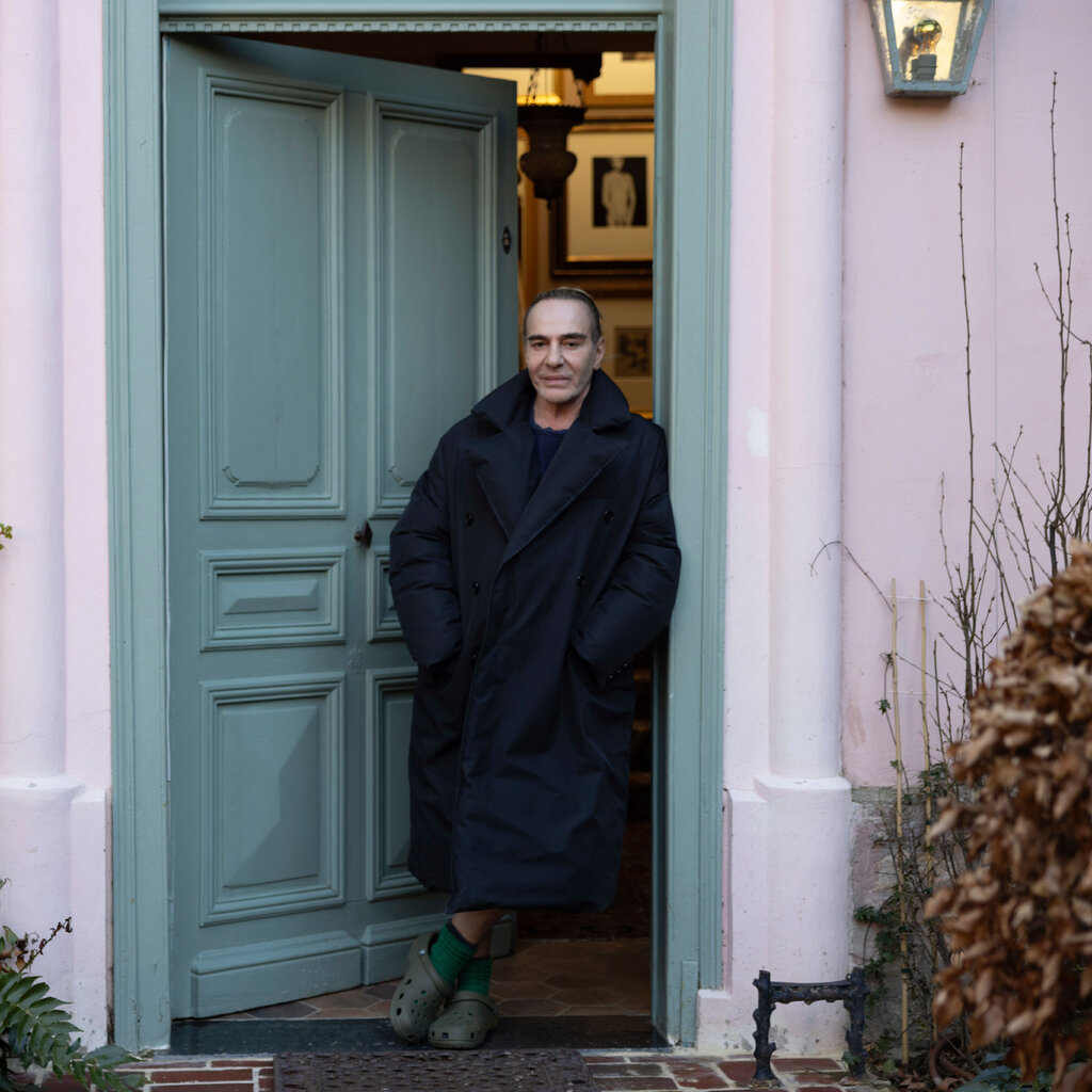 John Galliano in front of a light blue door in a pink wall. 