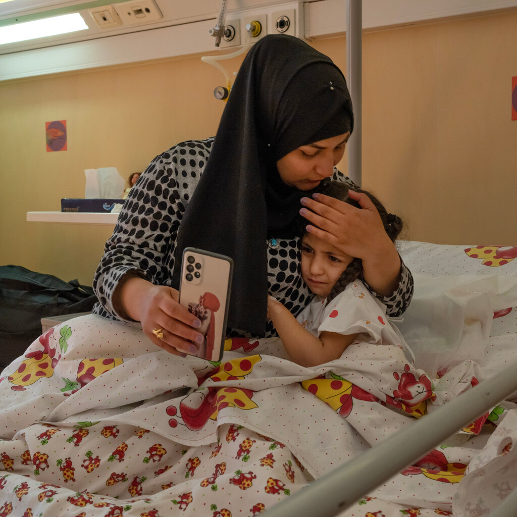 A woman sits beside a young girl in a hospital bed. 