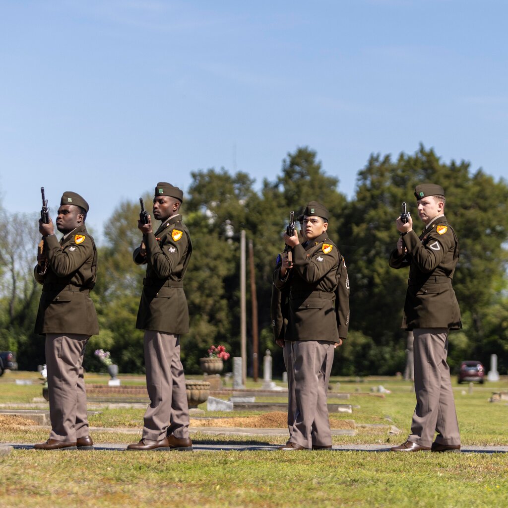 Four soldiers with rifles pointed in the air at a cemetery. 