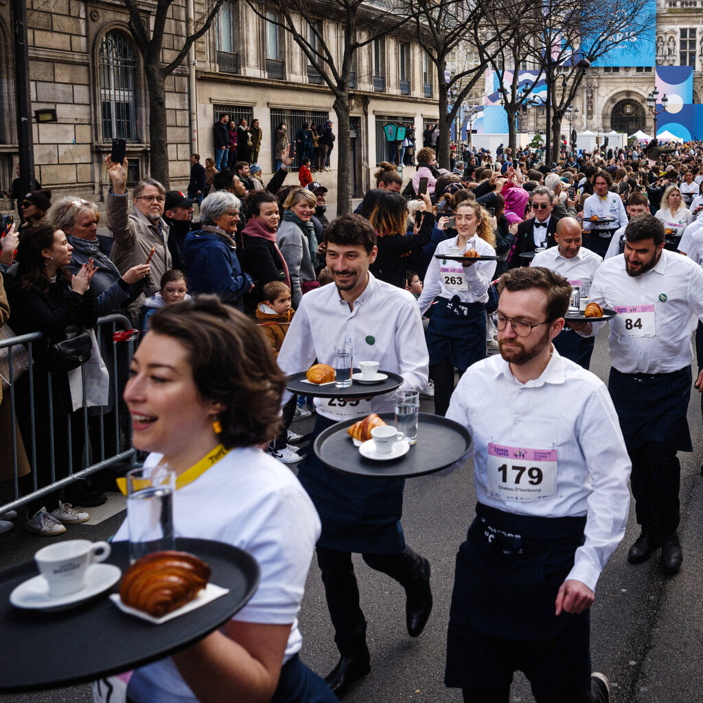 Waiters holding trays of croissants, coffee and water walk through the Paris streets. 