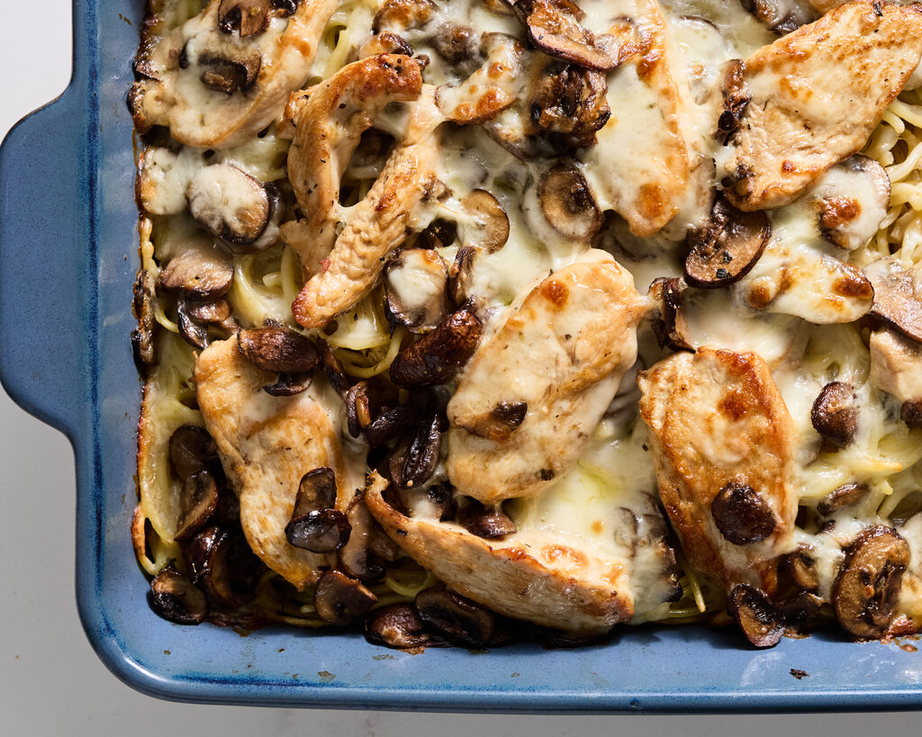 A top-down view of a casserole dish containing chicken, cheese, mushrooms and pasta. 