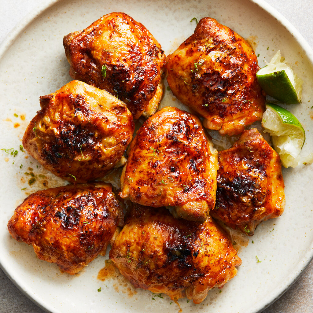 Seven roasted chicken thighs with hot honey and lime are on an ivory plate with squeezed lime wedges.