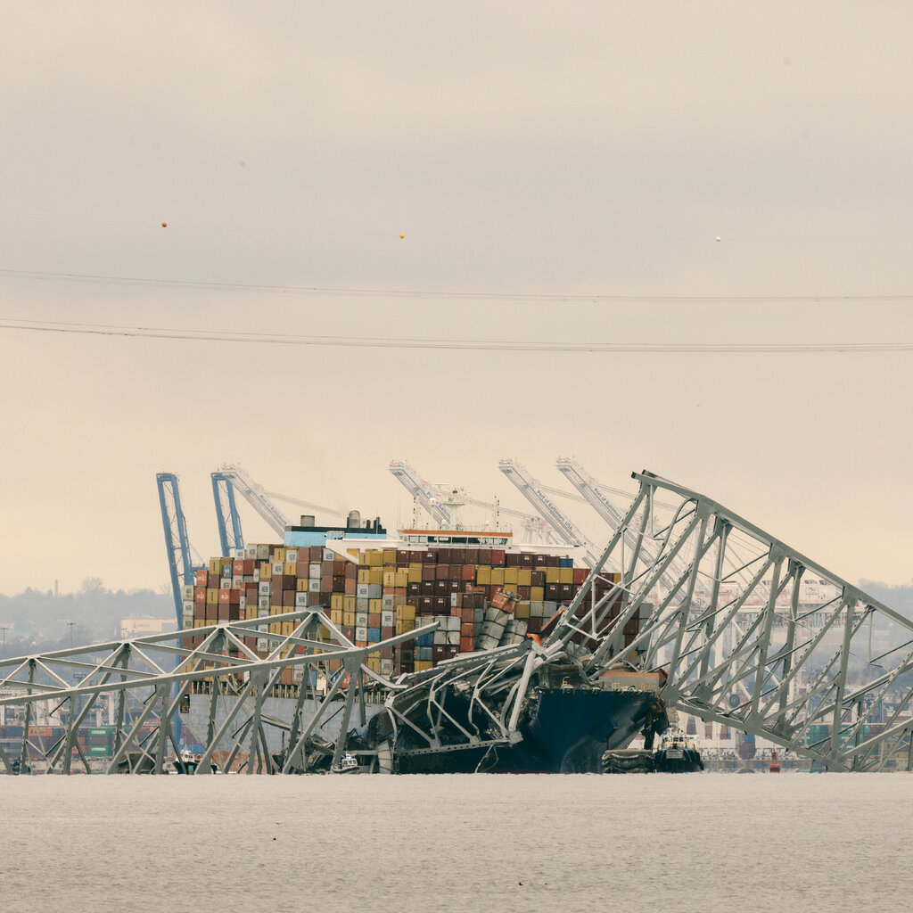 A twisted metal section of bridge is draped over a cargo ship.