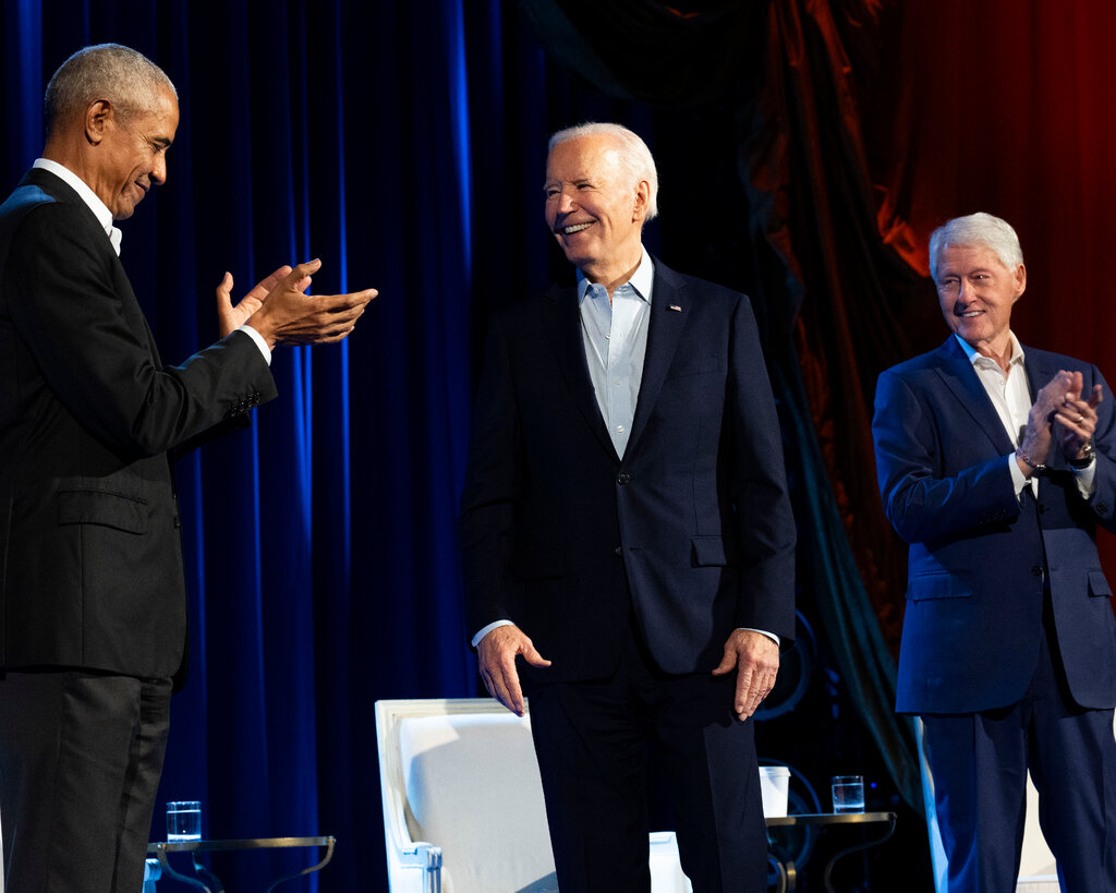 Barack Obama, President Biden and Bill Clinton stand onstage in suits without ties. 