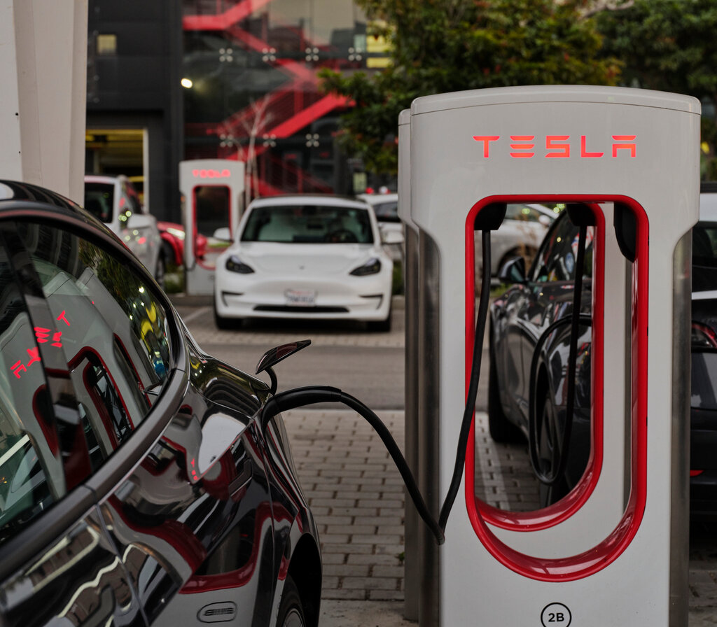 A Tesla charging station next to a black car. 