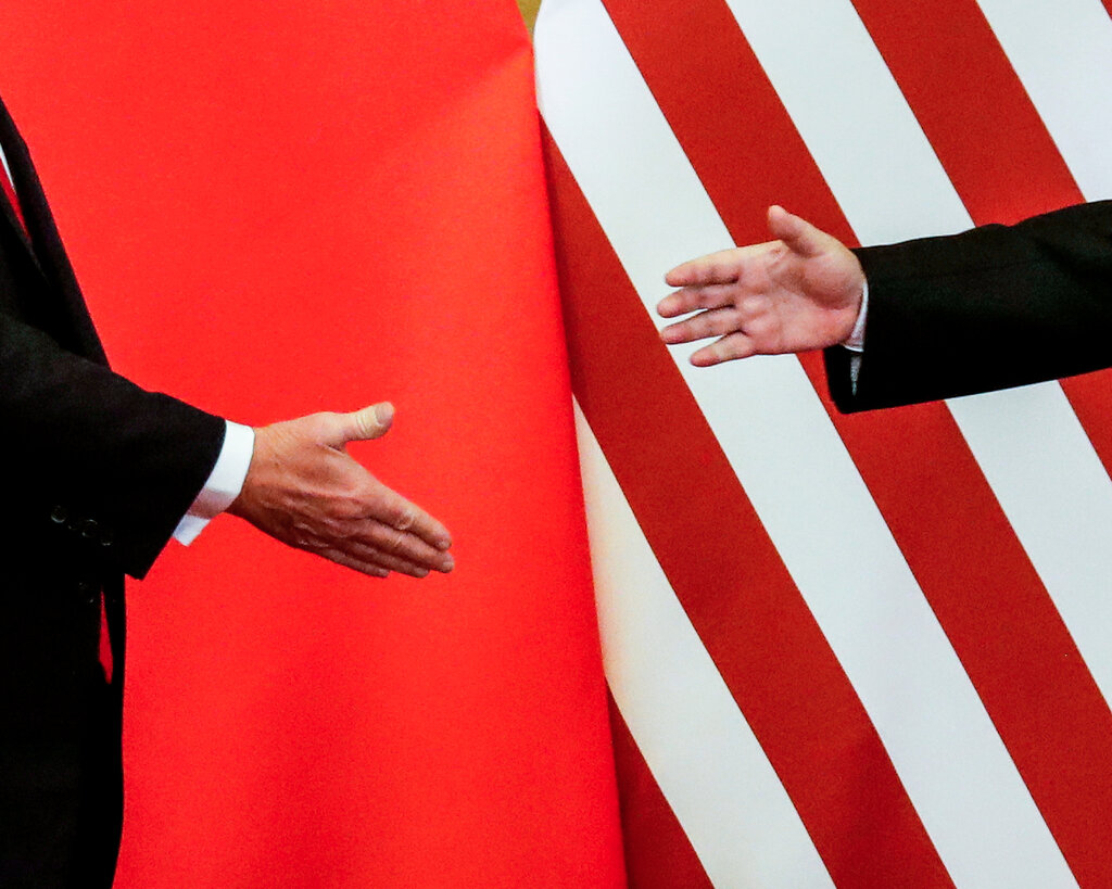 The arms of two leaders, Xi Jinping and Donald Trump, before a handshake.