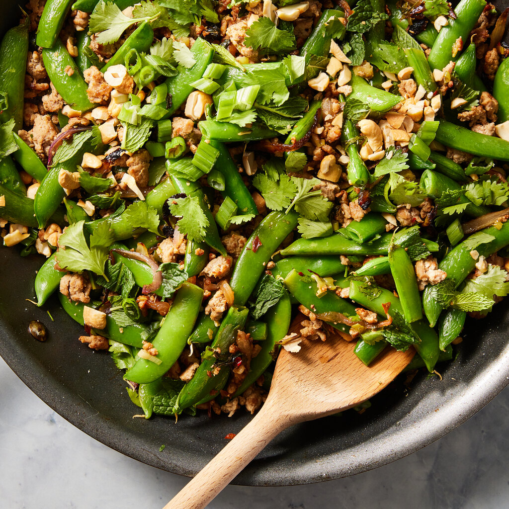 A skillet holds spicy ground turkey and snap peas scattered with chopped herbs.
