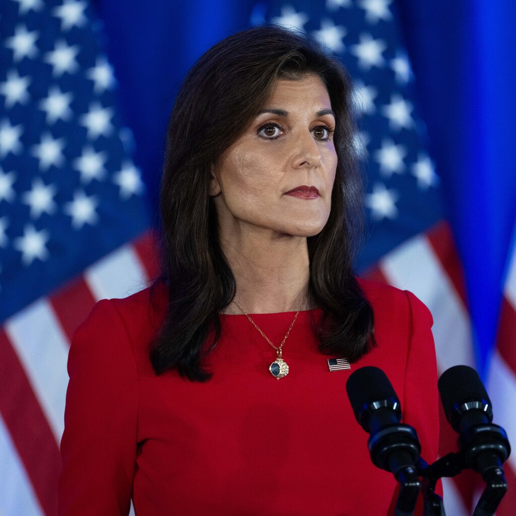 Nikki Haley, dressed in red, against a backdrop of flags.