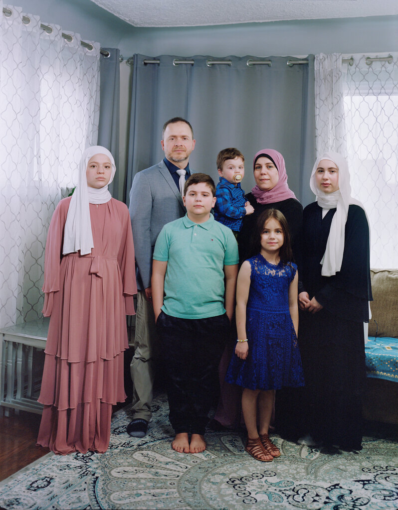Ahmad Al-Halabi with his wife, Rana, and their five children standing in the corner of a living room.