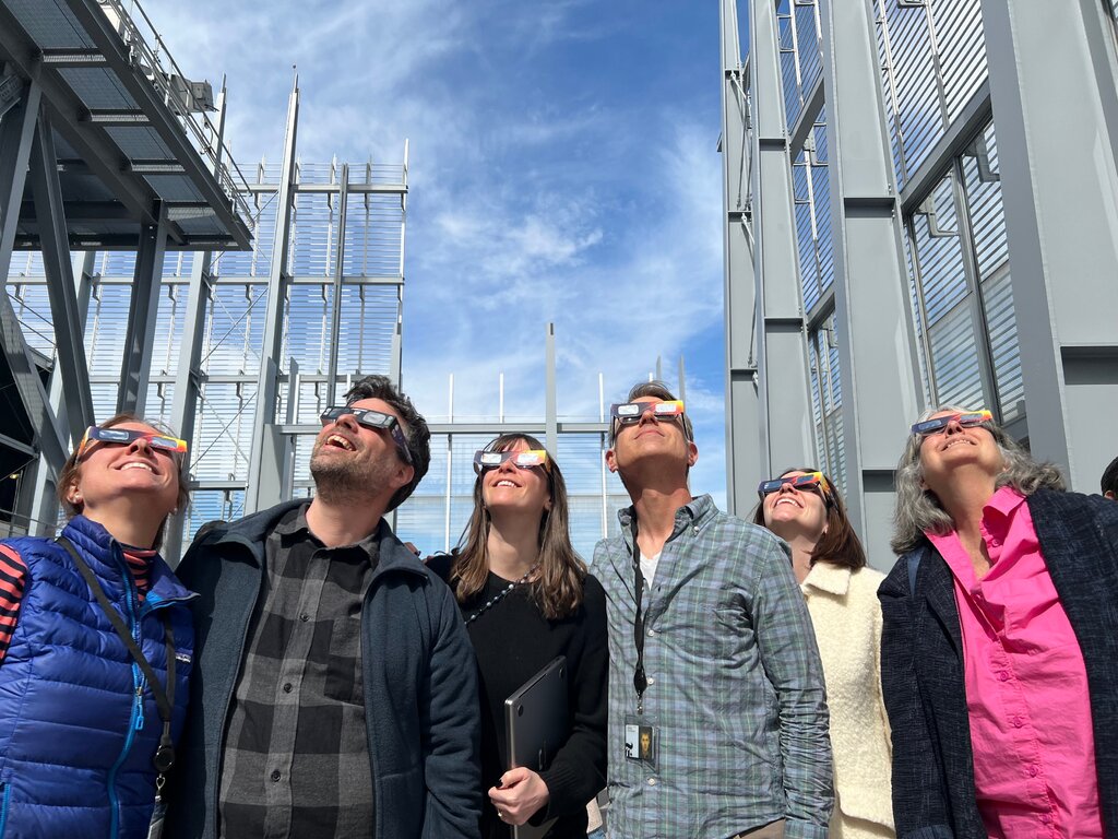 A group of people wearing eclipse glasses look up at the sky. 