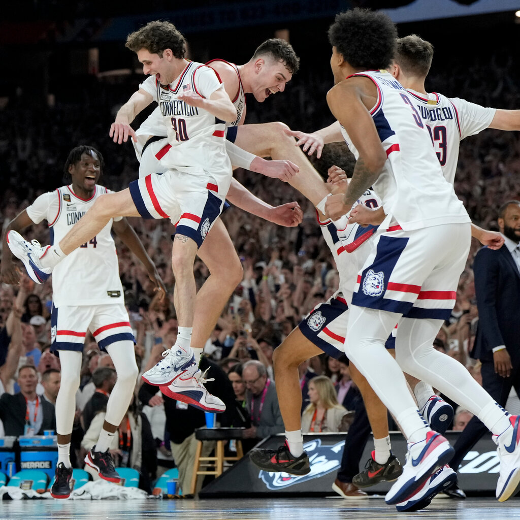 Members of a basketball team, wearing white uniforms, celebrate on a court. 