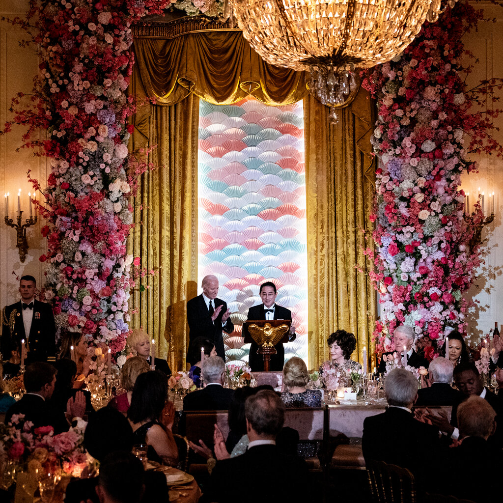 President Biden and Prime Minister Fumio Kishida of Japan stand in front of colorful fans, golden curtains and towering flowers. 