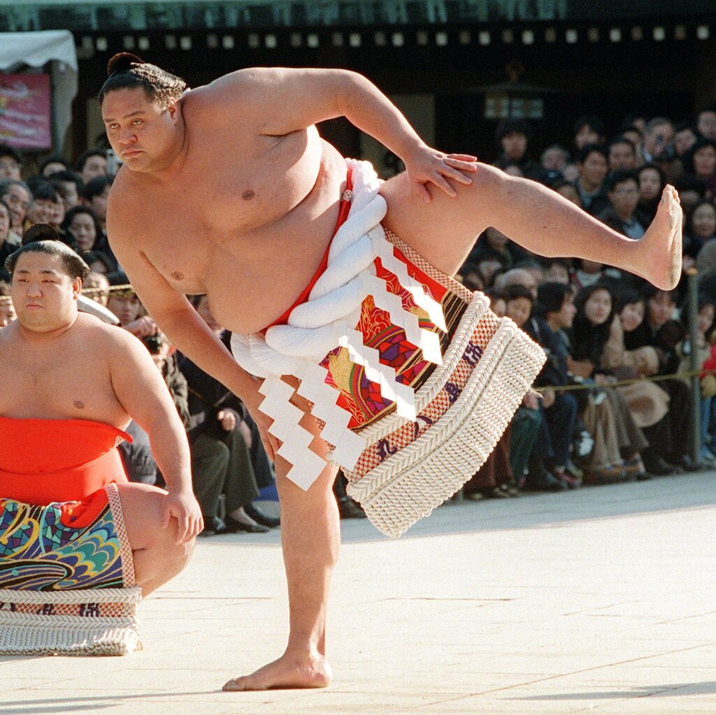 A sumo wrestler leans to his right while standing on one leg.