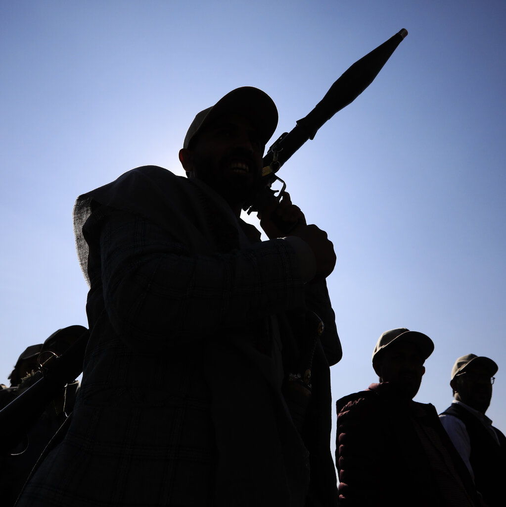 In a photograph shot from below, the silhouettes of men, one holding a weapon, against a bright blue sky.