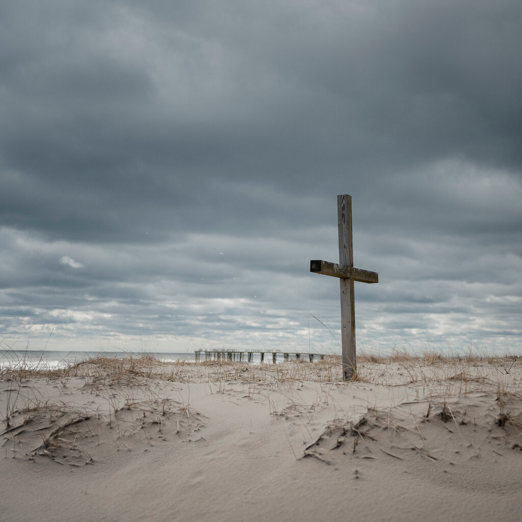 A beach, with a cross and a “keep off dunes” sign.