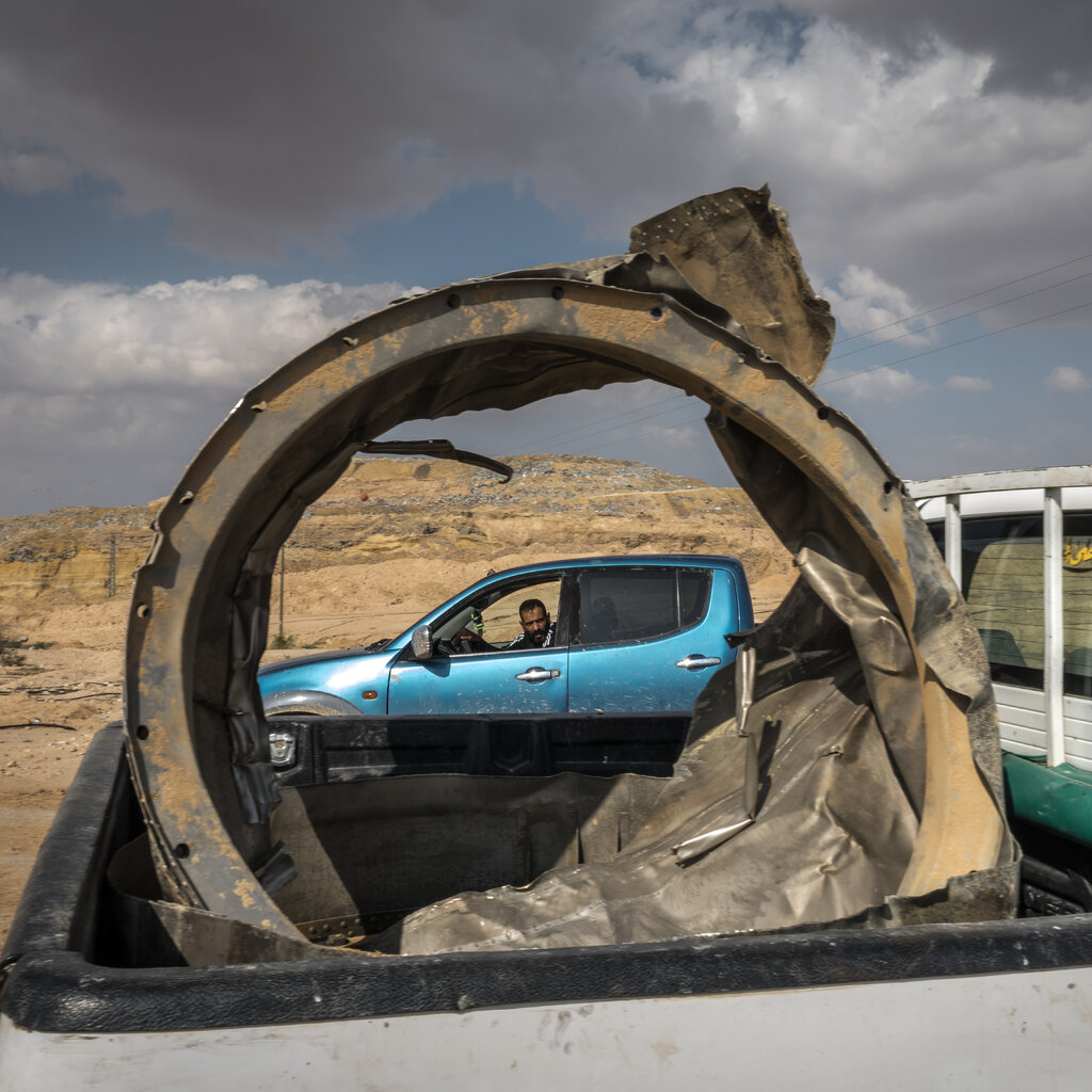 A large, warped metal cylinder in the back of a white pickup truck in a desert.