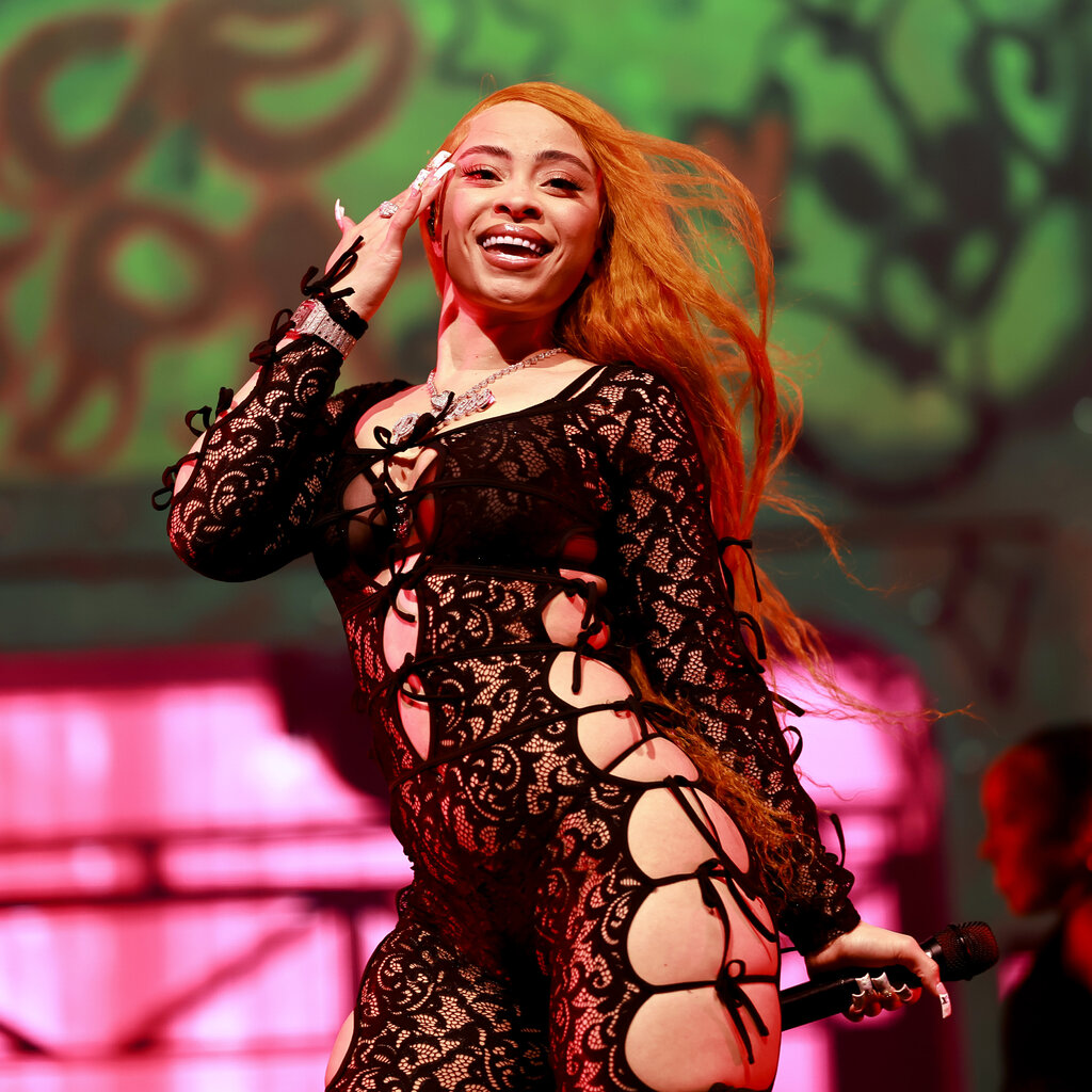 Ice Spice performing onstage in a black lacy bodysuit with ties on the legs, arms and chest.