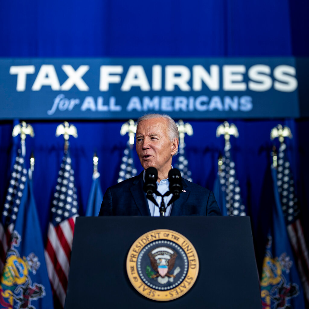 Joe Biden speaks at a lectern with the seal of the president on it. Behind me a sign reads: “Tax fairness for all Americans.”