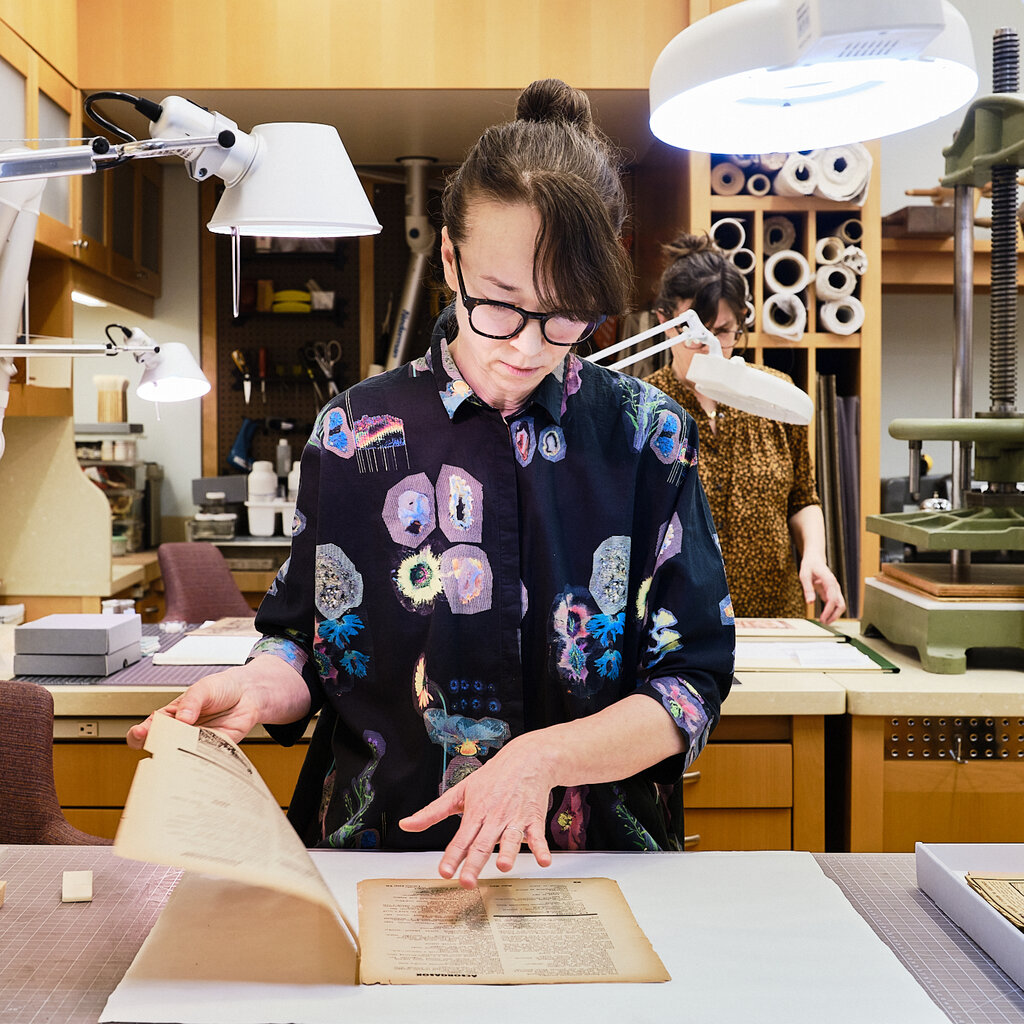 A conservator works on two leaves of aged paper. 