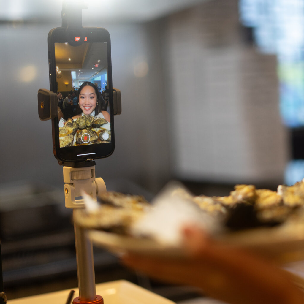 A phone on a stick holder records a woman holding up a plate of food. 