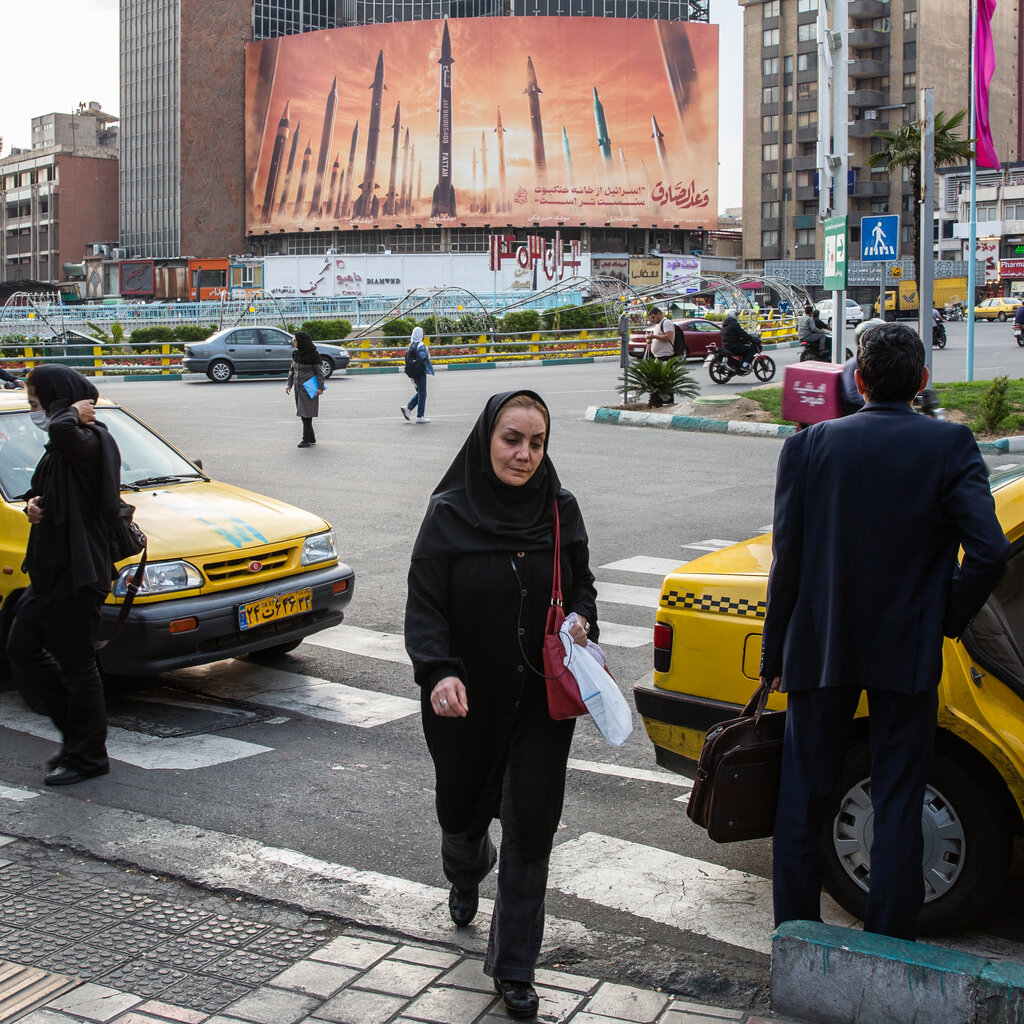 A city street in Tehran, in the background there’s a large poster with missiles on it. 