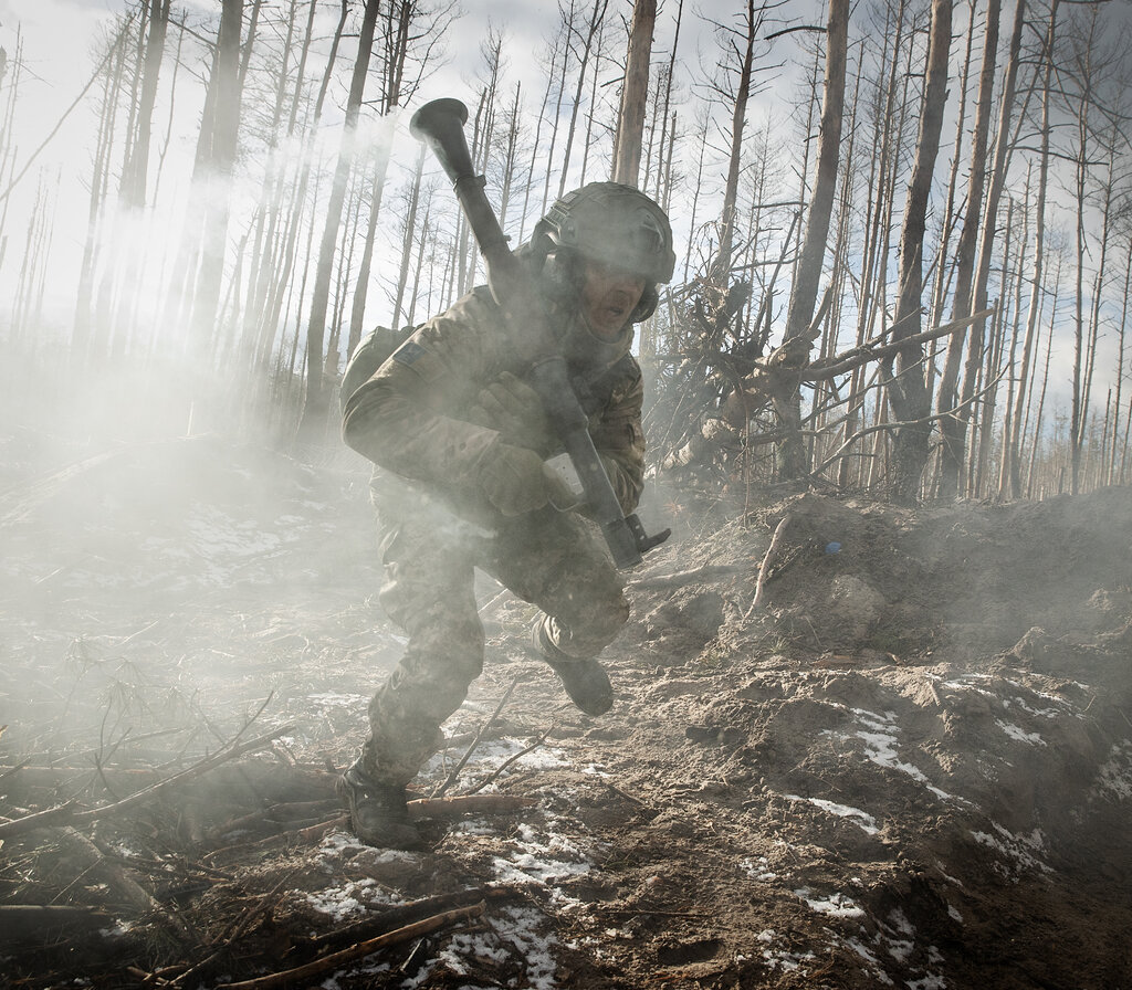 A soldier holding a grenade launcher runs through smoke in a forest.