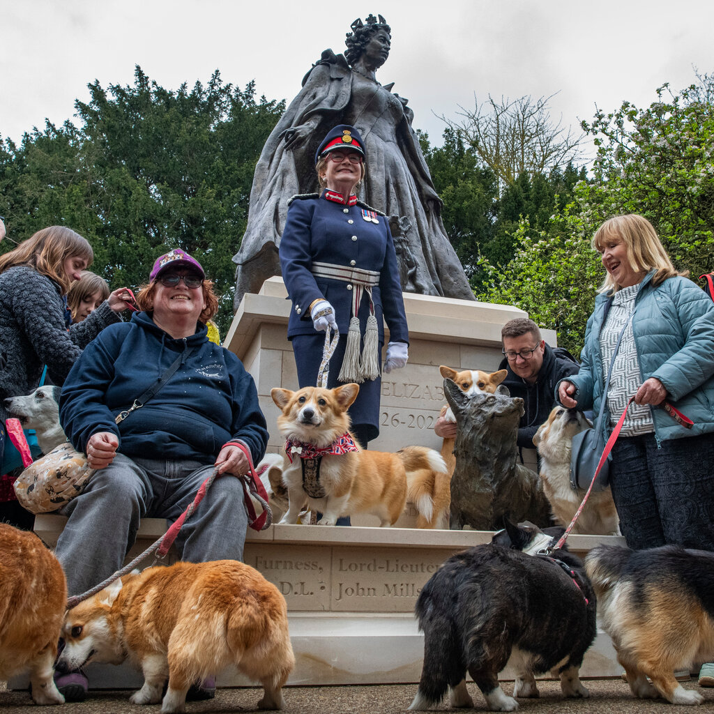 People with Corgis at the base of a statue of Queen Elizabeth II. 