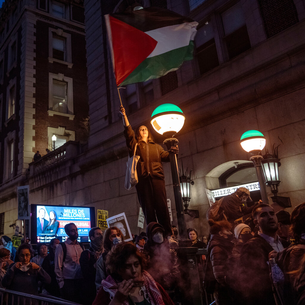 People take part in a protest in support of Palestine outside of Columbia University. One women stands on a subway entrance waving a Palestinian flag. 