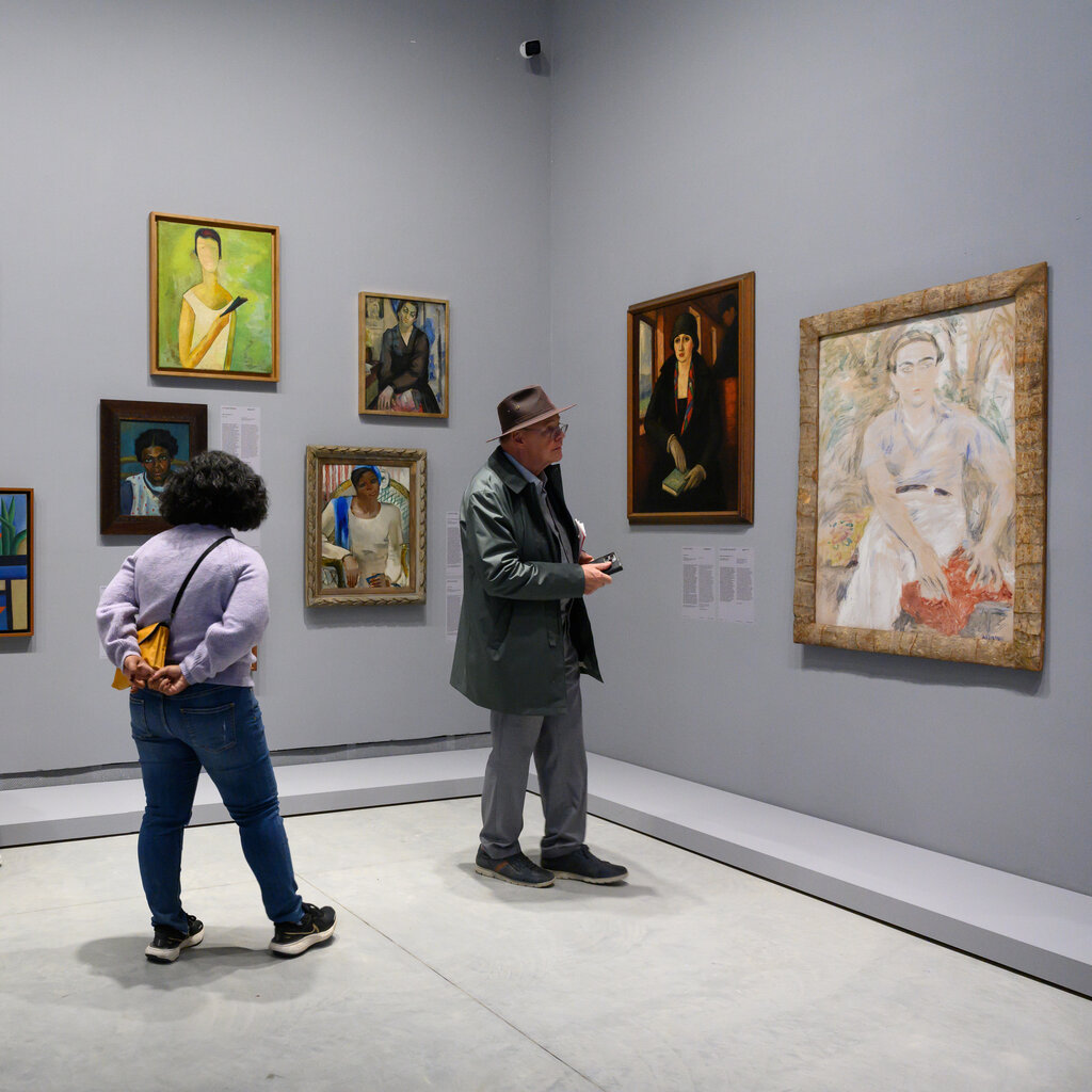 Visitors looking at a gray-walled gallery filled with portraits by various artists. 