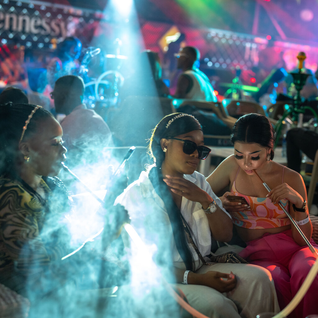 Women are seen smoking inside a bar filled with colorful lights.