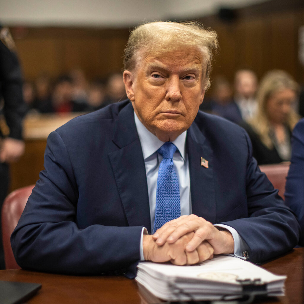Donald Trump sits at the defense table with his hands folded. 