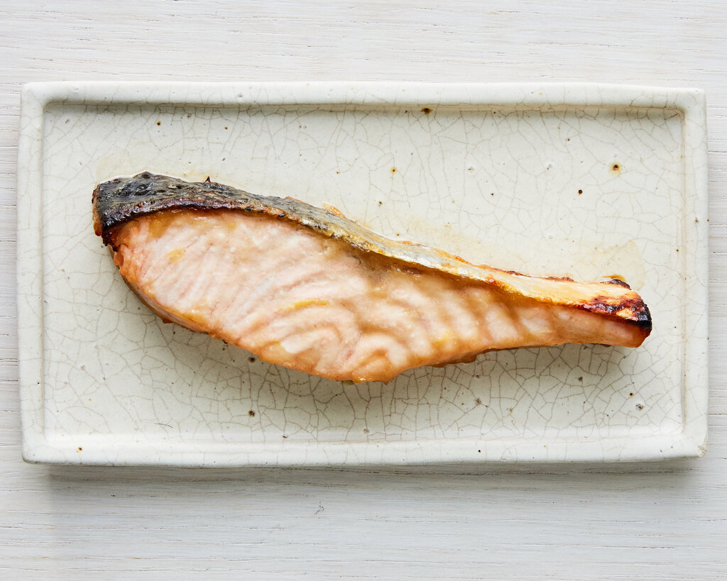 A piece of miso roasted salmon sits on a small rectangular dish.