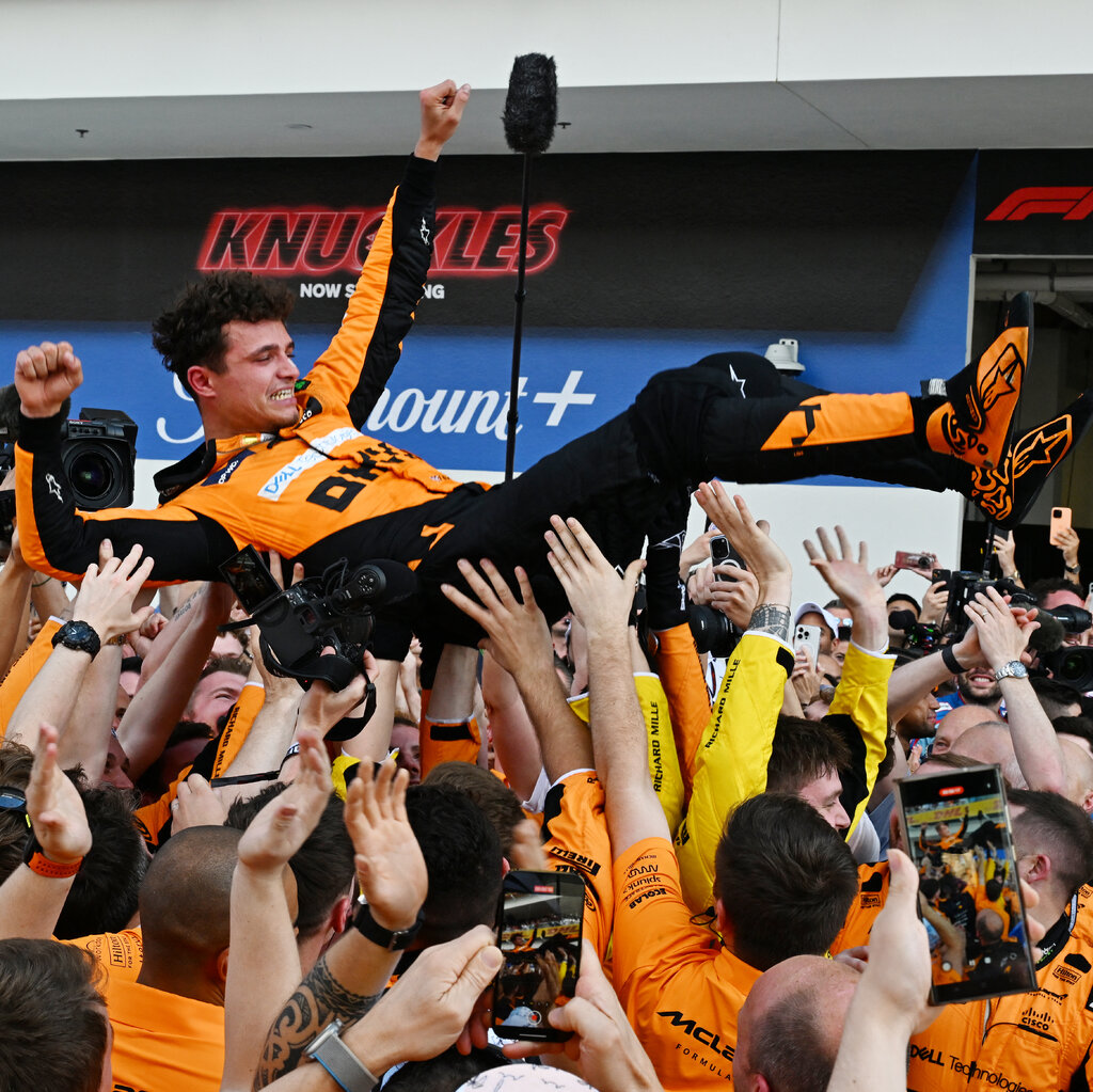 McLaren workers, dressed in orange, toss Lando Morris in the air. 