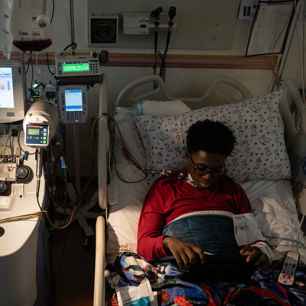 A preteen in a hospital bed, looking at a tablet.