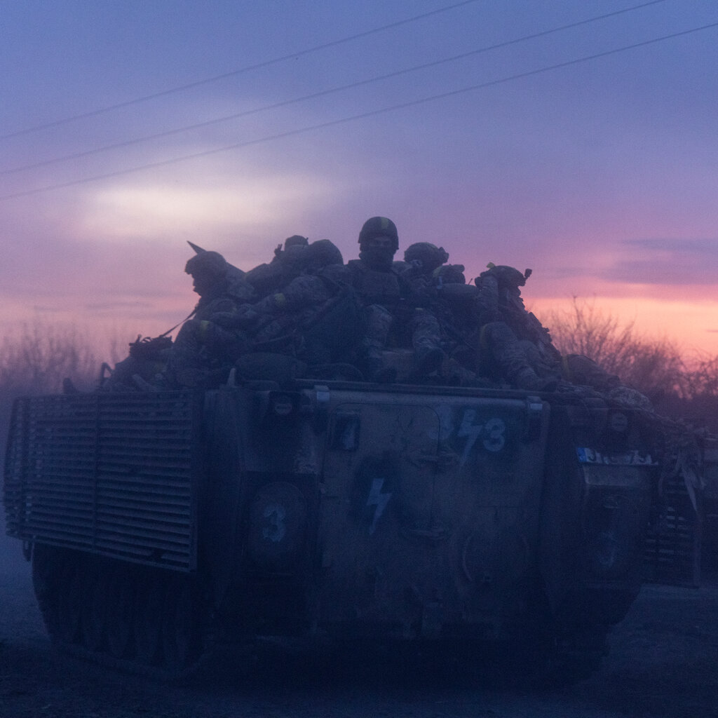 A group of soldiers on an armored vehicle at sunset.