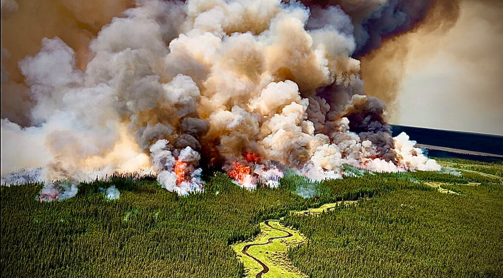 Reddish gray clouds of wildfire smoke billow over a forest.