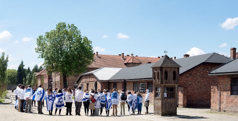 A group of youth draped in the Israeli flag visit Auschwitz.