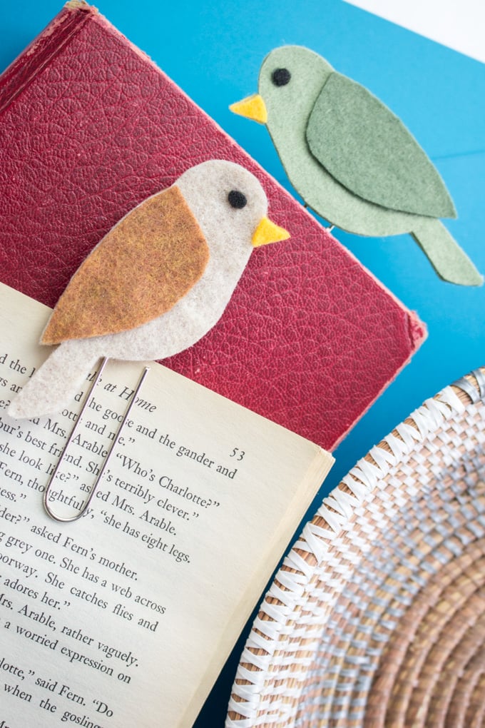 Two felt bird bookmarks place into a red leather book against a bright blue background.