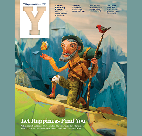 The winter 2023 Y Magazine cover illustrates a Don-Quixotic-type hiking character pausing to kneel in a mountain scene as a butterfly hovers above his outstretched hand. This supports the idea that happiness is something elusive and that our approach to finding it may be all wrong. Read expert insights on creating the good life. Illustration by Red Nose Studio.