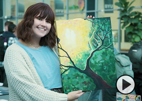A female BYU student proudly shows the painting she created for a BYU Foundations of the Restoration class..