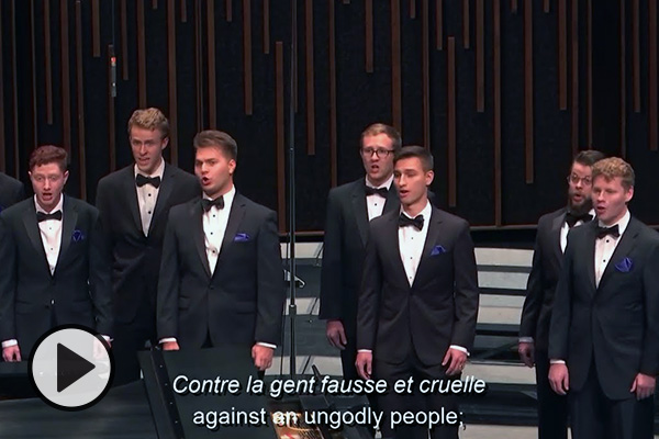 A screenshot from a BYU SIngers performance video. A group of men in black ties perform and the subtitle reads Contre la gent fausse et cruelle or against an ungodly people.