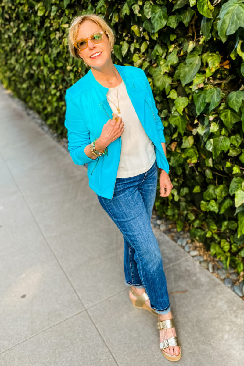 Susan B. of une femme d'un certain age wears an aqua knit moto jacket, jeans and gold sandals.
