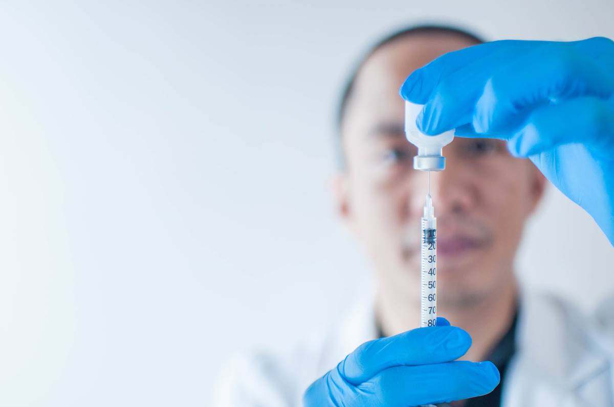 Foro colorida de um homem de luva se preparando para aplicar uma vacina - Metrópoles