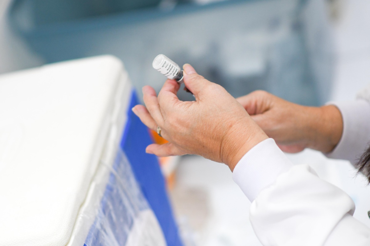 Imagem colorida de mãos femininas segurando frasco de vacina dengue - Metrópoles