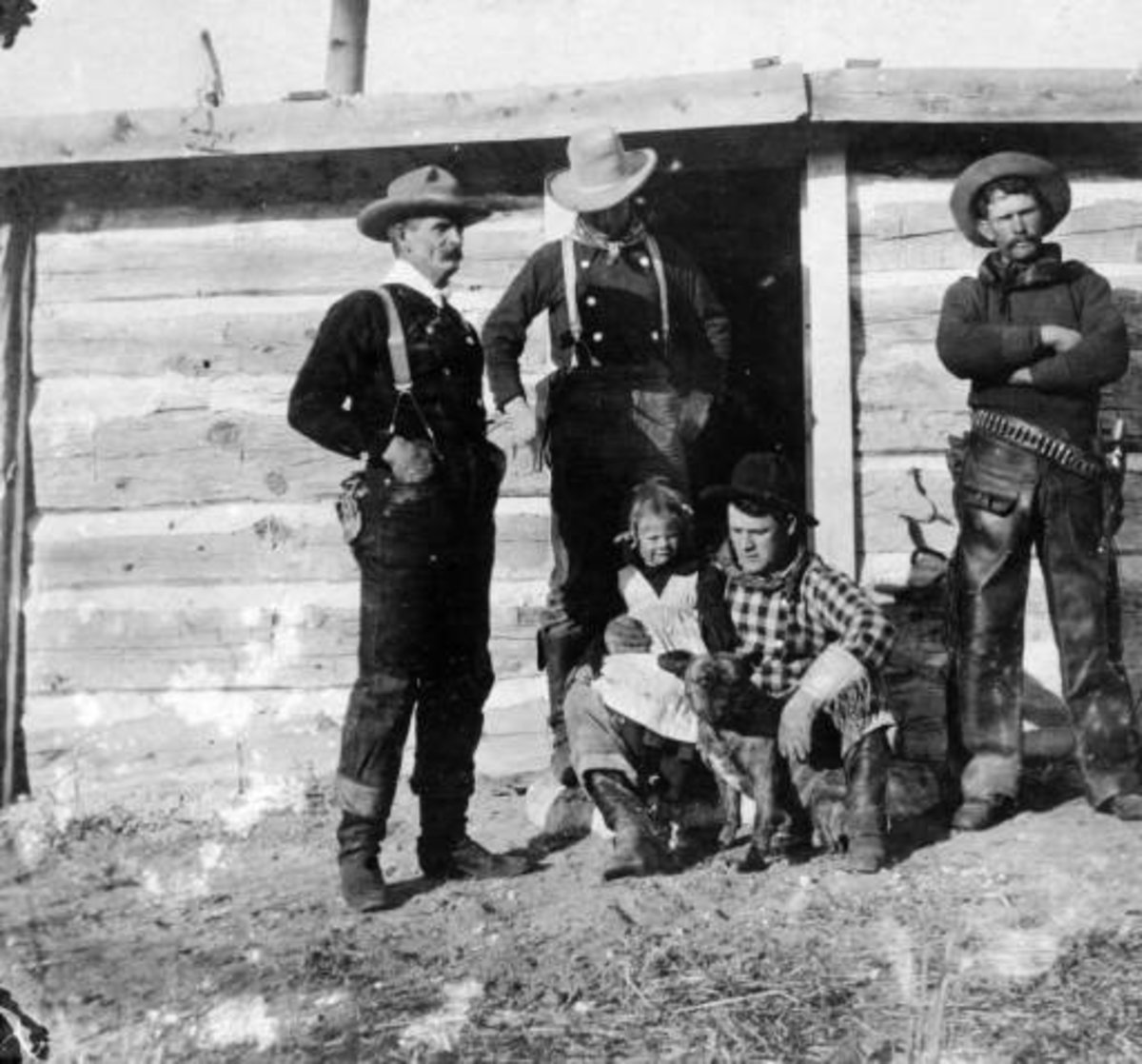 Real cowboys with a girl and a dog in Converse County, Wyoming; costume includes suspenders, bandanas, leather chaps, a pistol, holster, and ammunition belt. They are identified as: "Tom Black" "Chas Mayo" "Tex Biddick" and "Neal Hart a