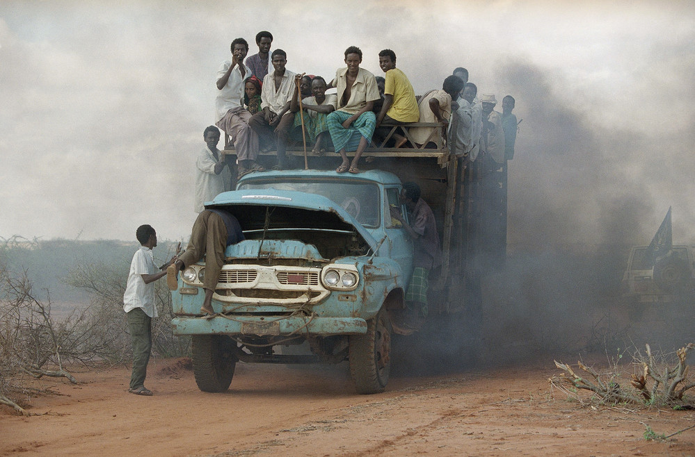 On this date in 1992: A group of Somalis crowd onto a broken-down truck, while one man checks under the hood, at the Mandera refugee camp in Kenya. The Somali Civil War, which is ongoing, continues to give rise to thousands of refugees.