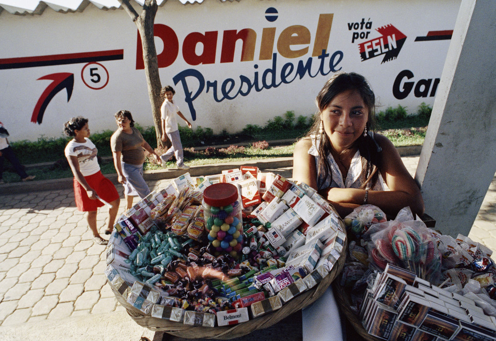 On this date in 1990: A young girl sells candies and bags of water in front of Sandinista party headquarters in Managua, Nicaragua. The headquarters was covered with political slogans promoting the candidacy of Nicaraguan President Daniel Ortega in preparation for a national election. Ortega was defeated by National Opposition Union candidate Violeta Chamorro, which led to a peaceful transfer of power in the country.